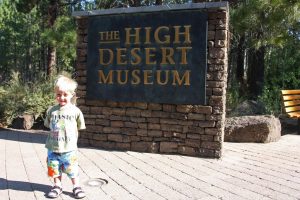 Happy child standing next to High Desert Museum sign